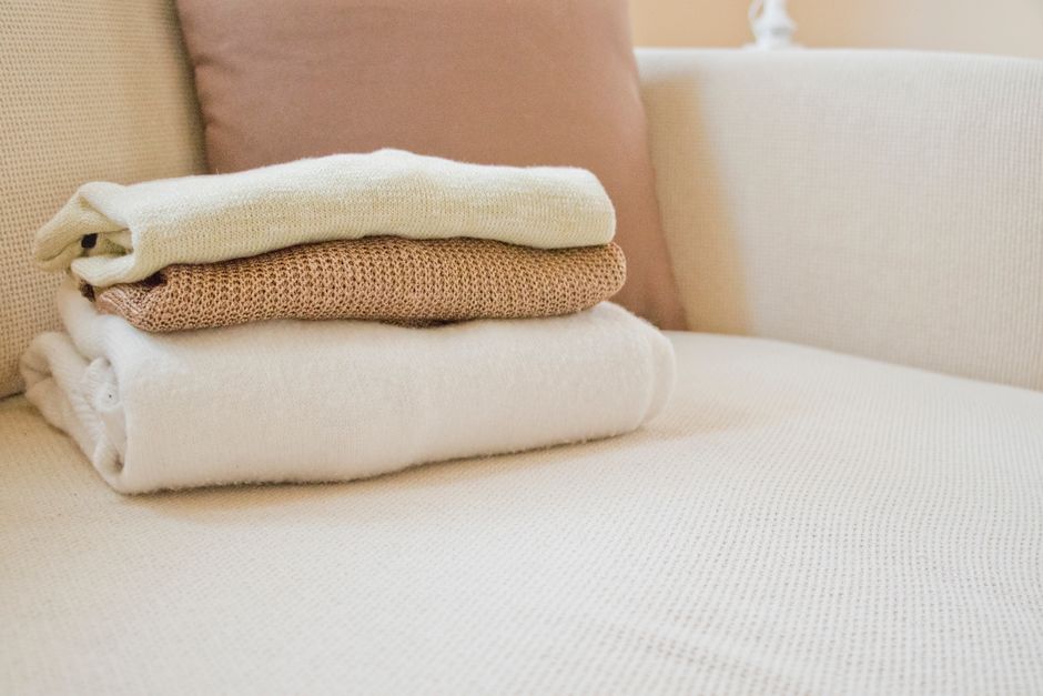 Sweaters doblados en tonos cálidos sobre un sofá crema