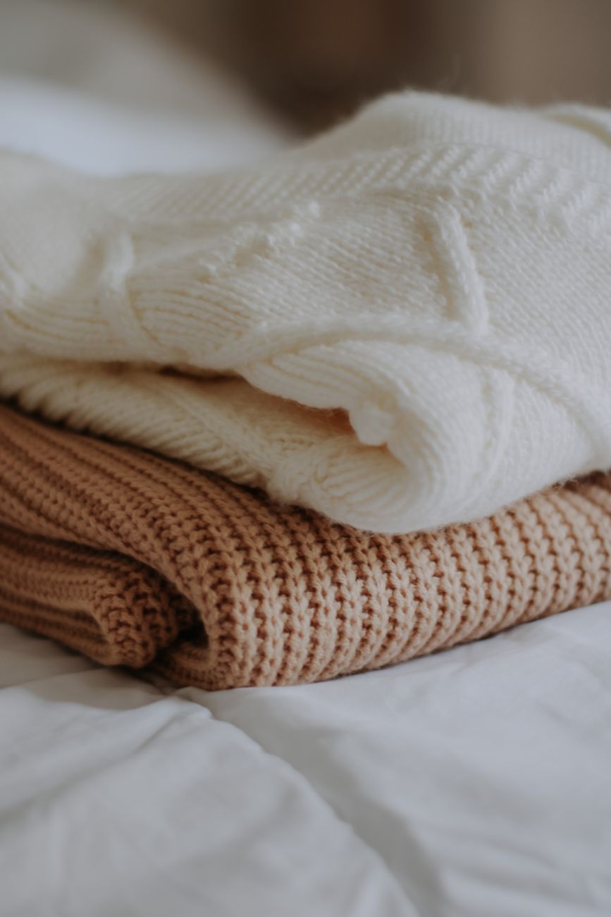 Sweaters de lana abrigados apilados sobre una cama