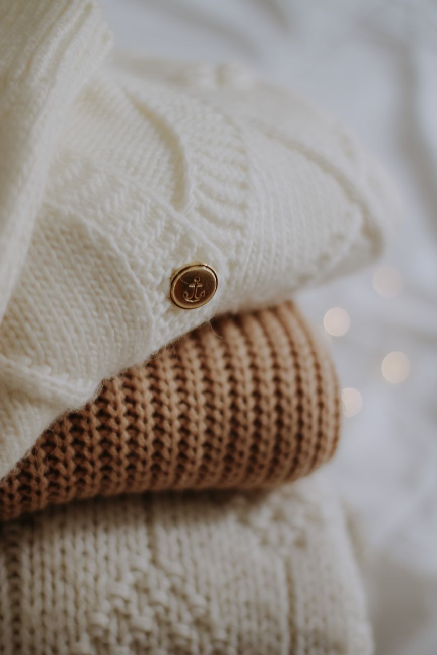 Pila de sweaters tejidos en tonos neutros y cálidos